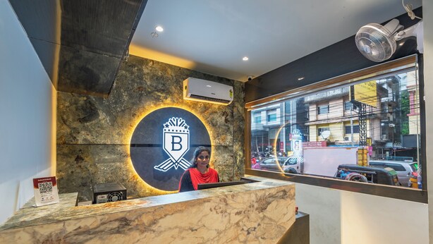 A reception desk with a marble top, a large circular logo with a 'B' and a bird, and an air conditioning unit above it. - Beverly Palace Kozhikode (Kozhikode)