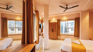 A hotel room with two beds, wooden furniture, a ceiling fan, and large windows. - Beverly Palace Kozhikode (Kozhikode)
