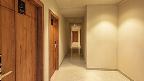 A hallway with wooden doors and a tiled floor, leading to a room with a door at the end. - Beverly Palace Kozhikode (Kozhikode)