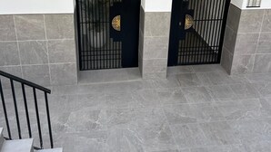 A staircase leading to two black gates with decorative symbols, set against a wall with grey tiles. - Torremolinos Center, Magnificent Air-conditioned Apartment, Wifi, Beautiful (Torremolinos)