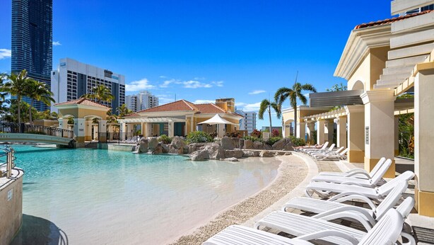 A resort pool area with lounge chairs, a small building, and a clear blue sky.