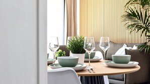 A dining area with a round table set for two, featuring green plates, white bowls, and clear wine glasses.