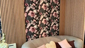 Ein modernes Wohnzimmer mit einer gebogenen Couch, Holzboden und floralem Wandpapier.