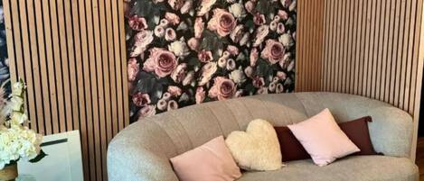 Una sala de estar moderna con un sofá curvo, piso de madera y papel tapiz floral.