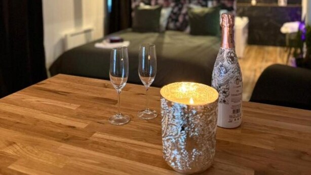 Ein Hotelzimmer mit Holztisch, zwei Weingläsern, einer Kerze und einer Champagnerflasche.