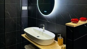 Ein modernes Badezimmer mit einem großen, ovalen Waschbecken, schwarzen Marmorwänden und einer Holzboden.