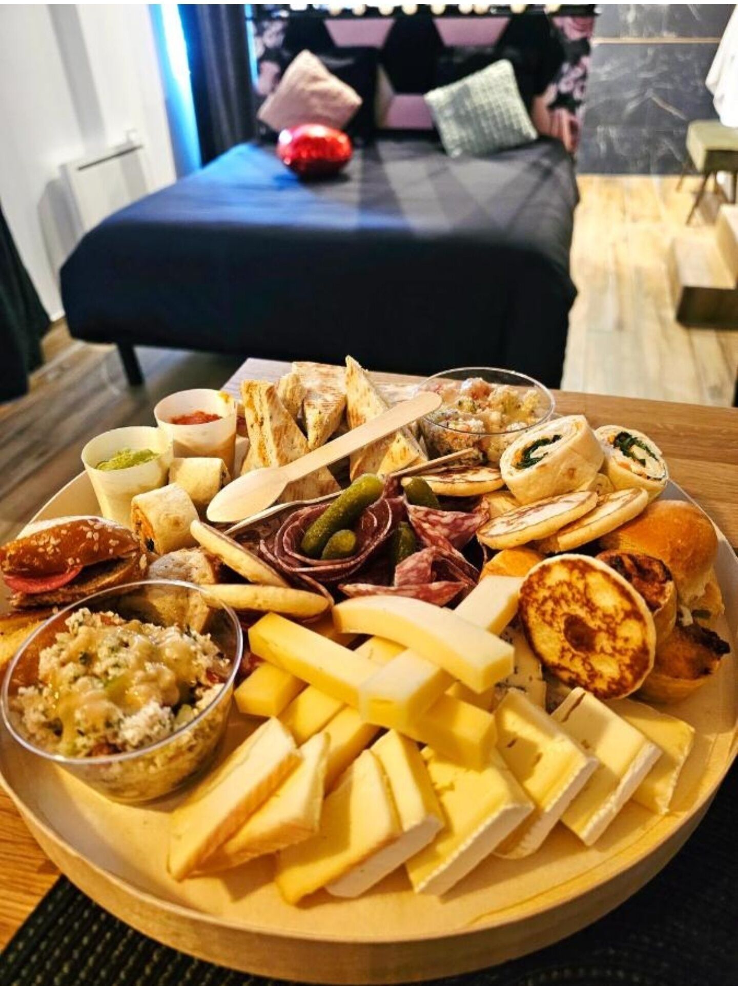 A charcuterie board with various cheeses, meats, and pickles on a wooden table in a hotel room.