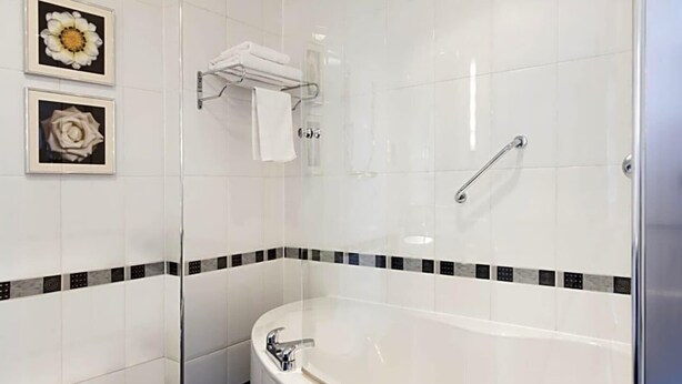 Une salle de bain moderne dotée d’une douche à parois de verre, d’une baignoire sur pieds et de deux tableaux floraux encadrés accrochés au mur.