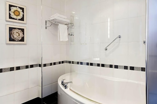 Une salle de bain moderne dotée d’une douche à parois de verre, d’une baignoire sur pieds et de deux tableaux floraux encadrés accrochés au mur.