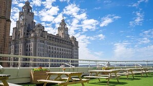 Terraza en la azotea con mesas de picnic y vistas a un edificio histórico.