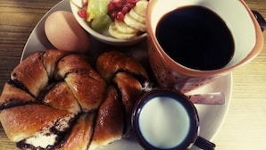 A plate with a pastry, a bowl of fruit, a cup of coffee, and a small bowl of cream. - Kiwi Backpackers Hostel (Pokhara)