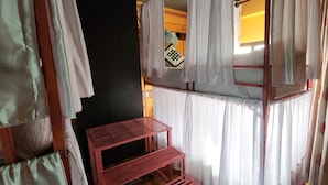 A room with a bunk bed, white curtains, a small red shelf, and a wall with a decorative item. - Kiwi Backpackers Hostel (Pokhara)