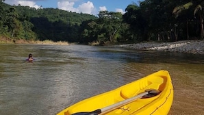 Een gele kajak met peddel en reddewest op de oever van een rivier.
