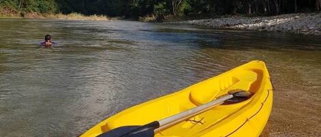 A yellow kayak with a paddle and a life jacket on the shore of a river.