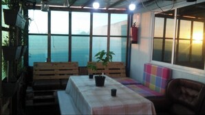 A cozy indoor seating area with wooden benches and a table, a potted plant, and a view through large windows. - Bungalow by the sea Cozy We accept pets (Costa da Caparica)