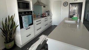 A modern kitchen with white cabinetry, a stainless steel refrigerator, a built-in oven, and a large island with a sink.