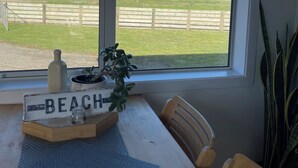 A room with a large window overlooking a grassy field and a mountain. There is a wooden table with a tray labeled "BEACH" and a potted plant.