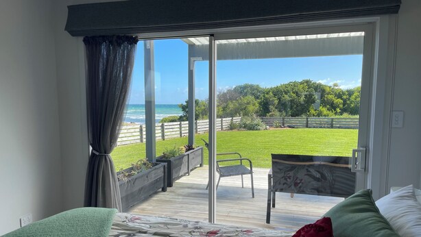 A bedroom with a bed, a green throw, a floral bedspread, and a view of a grassy yard and ocean through a sliding glass door.