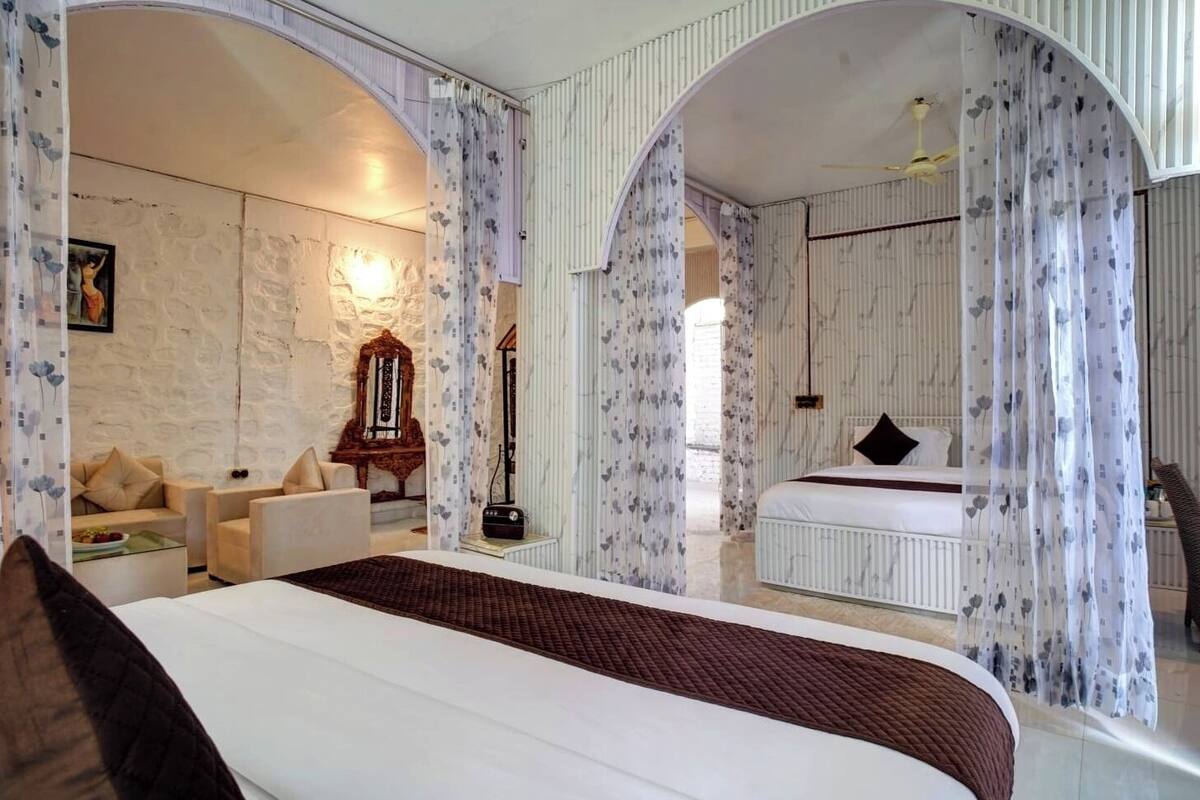 A bedroom with a large bed, a sitting area with a sofa and armchairs, a mirror, and a radiator.