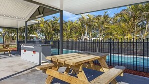 A covered outdoor area with picnic tables, a pool, and a building in the background. - Palm Valley Motel (Tarro)