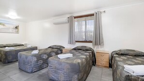 A room with four beds, a wooden dresser, a window with curtains, and an air conditioning unit. - Palm Valley Motel (Tarro)