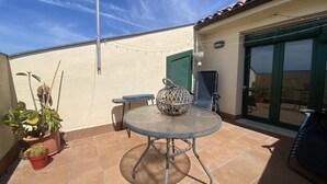 Un patio con una mesa redonda y sillas, plantas en macetas y una guirnalda de luces.