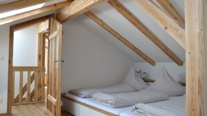 Una habitación pequeña y acogedora con techo inclinado y vigas de madera, que incluye una cama individual con ropa de cama a cuadros y una mesita de noche sencilla.
