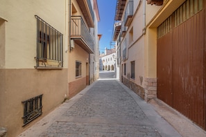 A narrow cobblestone street between buildings with barred windows and a closed wooden door.