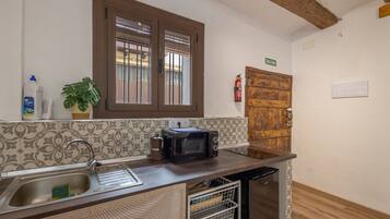 Una cocina con un lavamanos, un tostador, una planta en maceta, un extintor y una puerta de madera con la inscripción 'SALIDA'.