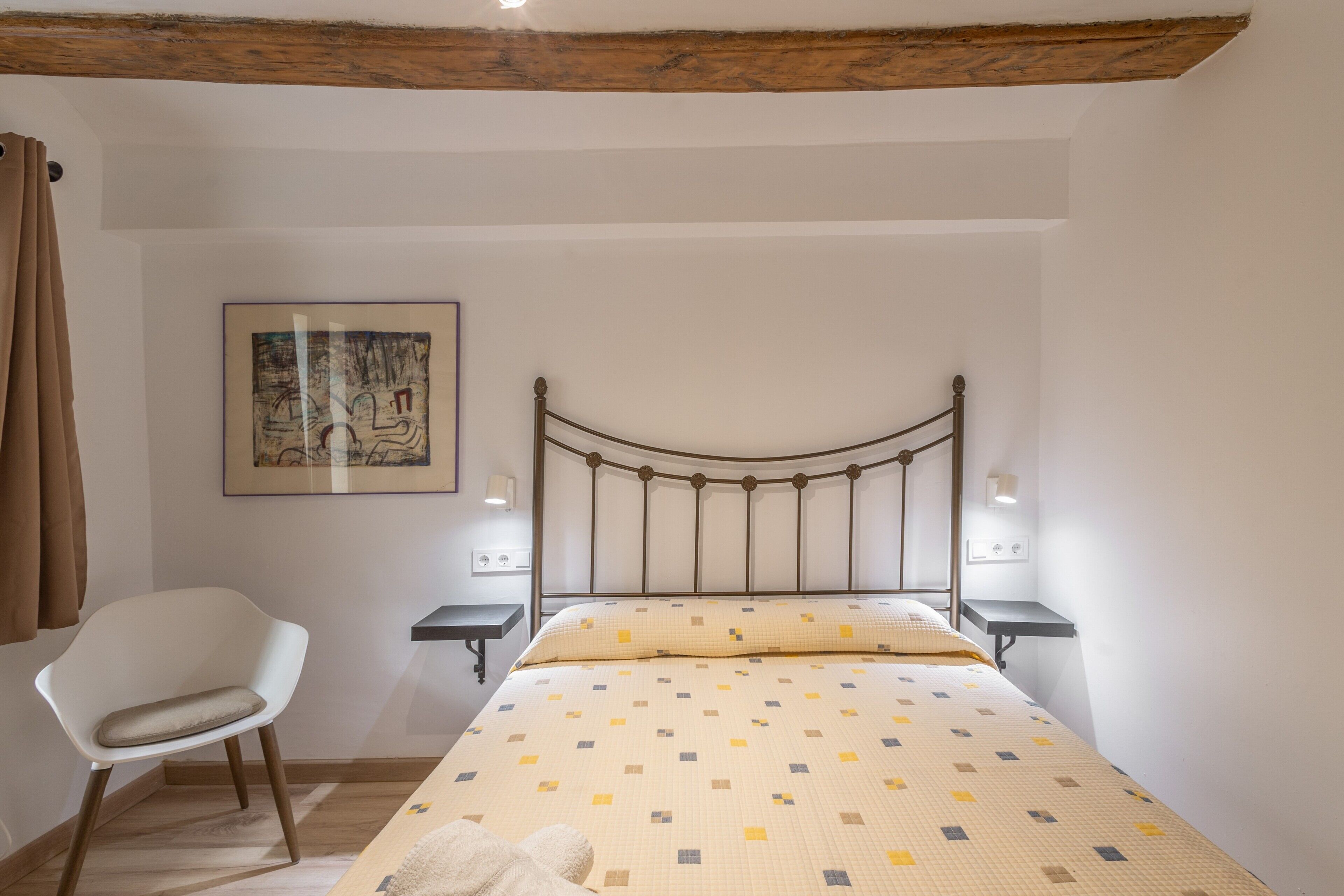 Ein Schlafzimmer mit einem Bett, einem Sessel, einem Nachttisch, einer Wandleuchte und einem gerahmten Bild.