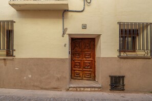 A building with a wooden door, a small window with metal bars, and a number plate above the door. - Studio 'Mayor 10' in Ejulve (Ejulve)
