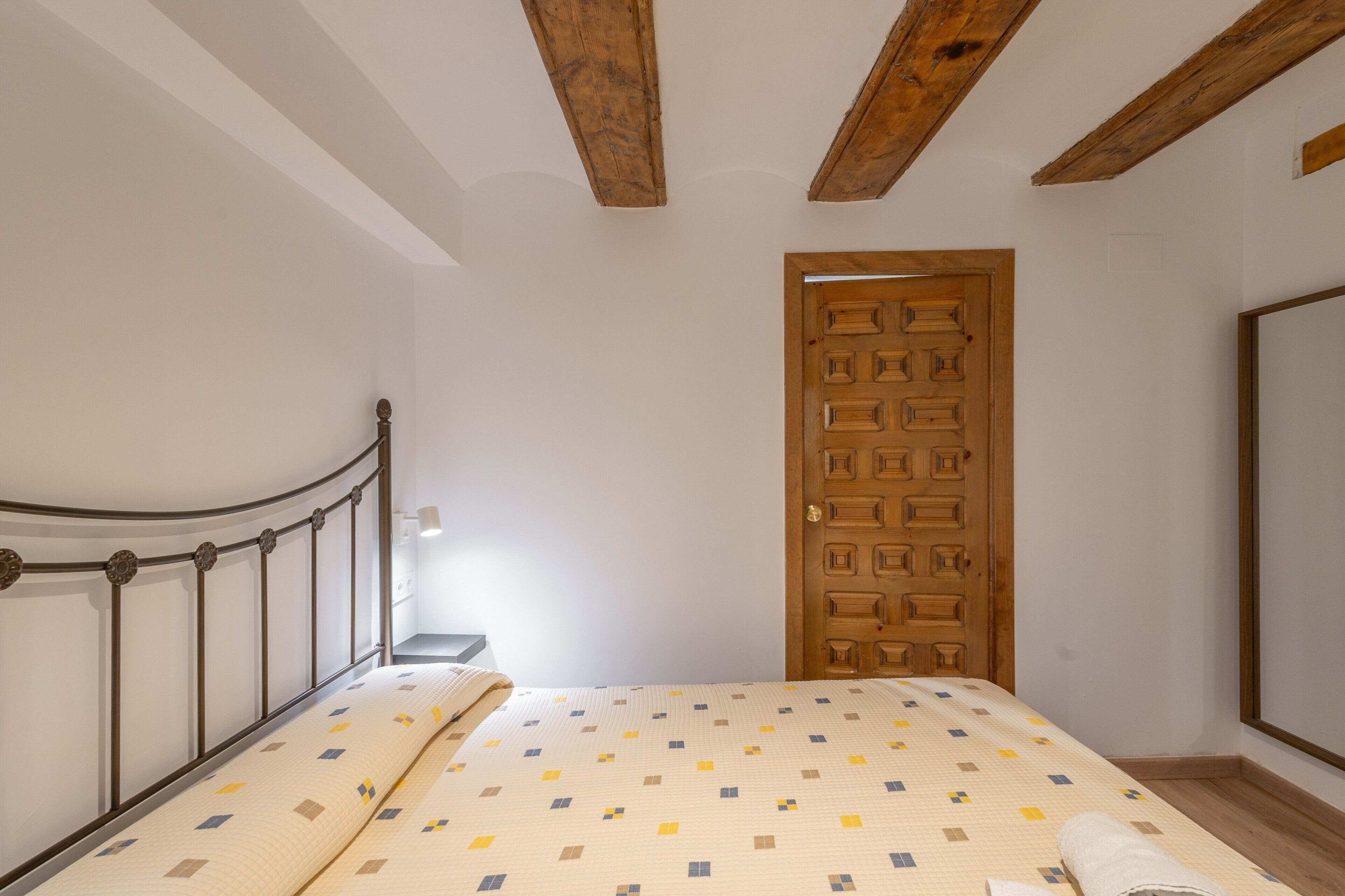 A bedroom with a bed, a wooden door, and a white wall.