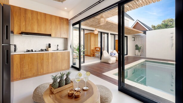 Una cocina moderna con armarios de madera, un comedor con mesa redonda de madera y vistas a una piscina a través de puertas de vidrio grandes.