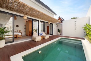 Een modern buitenzwembad met een houten terras, een slaapkamer met glazen wanden, en een witte buitenmuur.