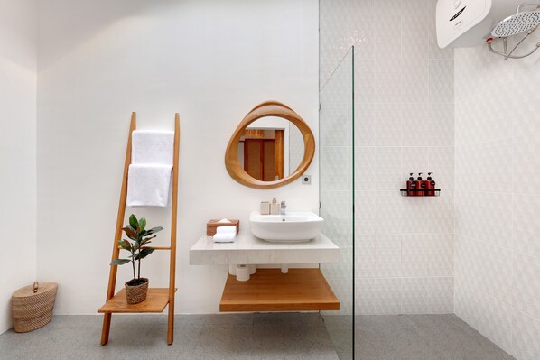 Une salle de bain moderne avec un meuble-lavabo en bois, un miroir rond, une cabine de douche en verre et une petite plante posée sur une étagère.