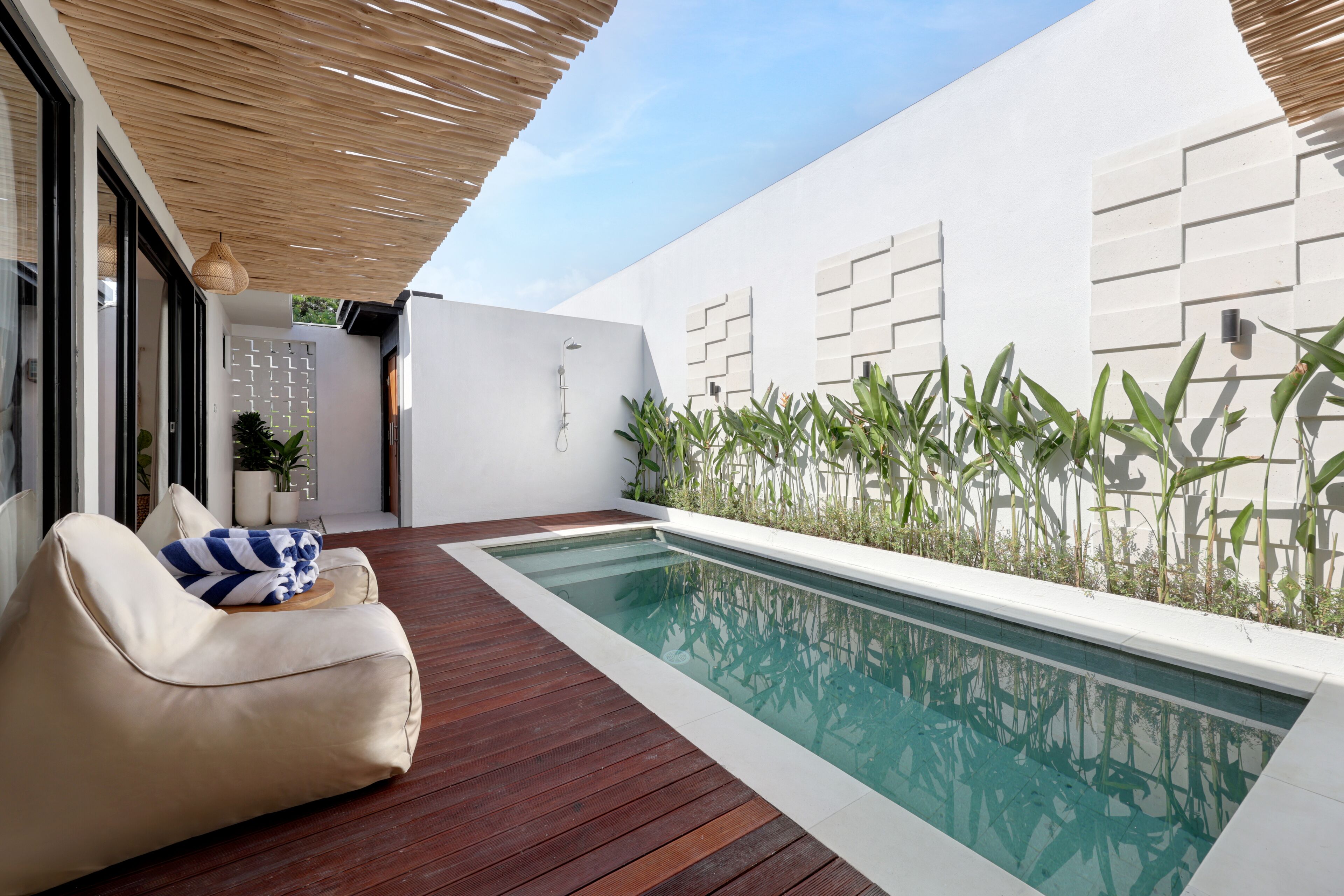 A modern outdoor pool area with a wooden deck, a beige lounge chair, and a white wall with geometric patterns.