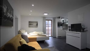 A modern living room with a sofa, a bed, a kitchen area, and a dining table.