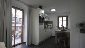 A modern kitchen with white cabinets, a built-in oven, and a dining area with a table and chairs.