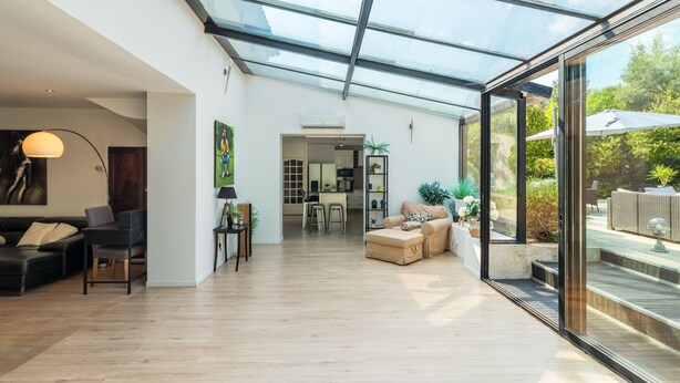 Un'ampia zona giorno con soffitto in vetro, un divano, un tavolo da pranzo e una cucina sullo sfondo.