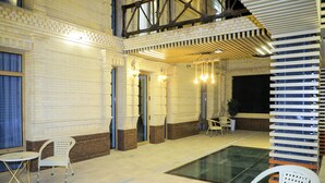 Un vaste espace intérieur doté d’une piscine, de chaises blanches et d’un haut plafond avec des poutres apparentes.