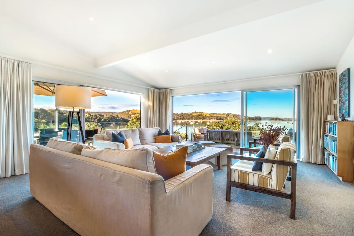 A spacious living room with a large sofa, a coffee table, and a view of a scenic landscape through large windows.