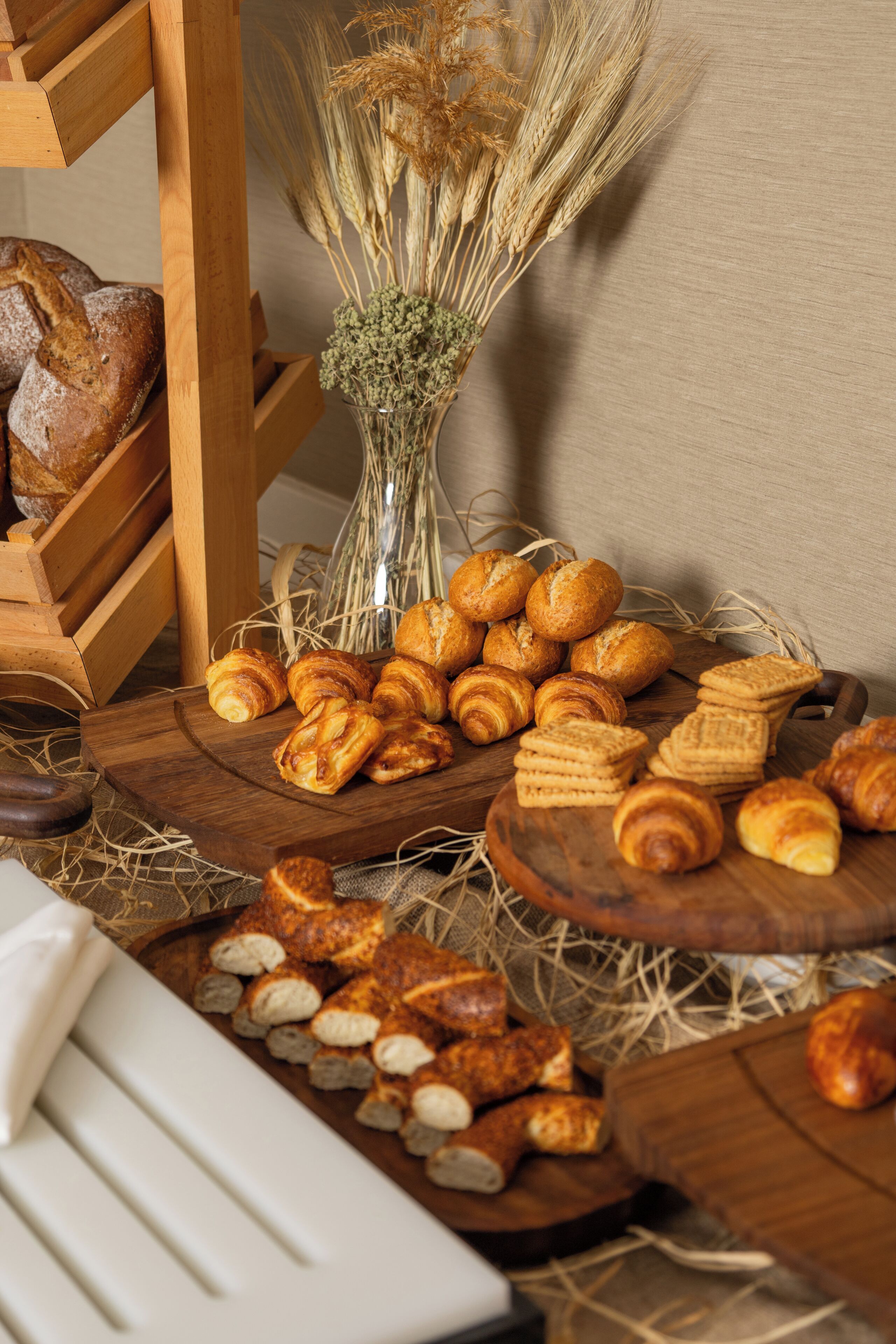 A wooden table with pastries, a vase with dried plants, and a loaf of bread.
