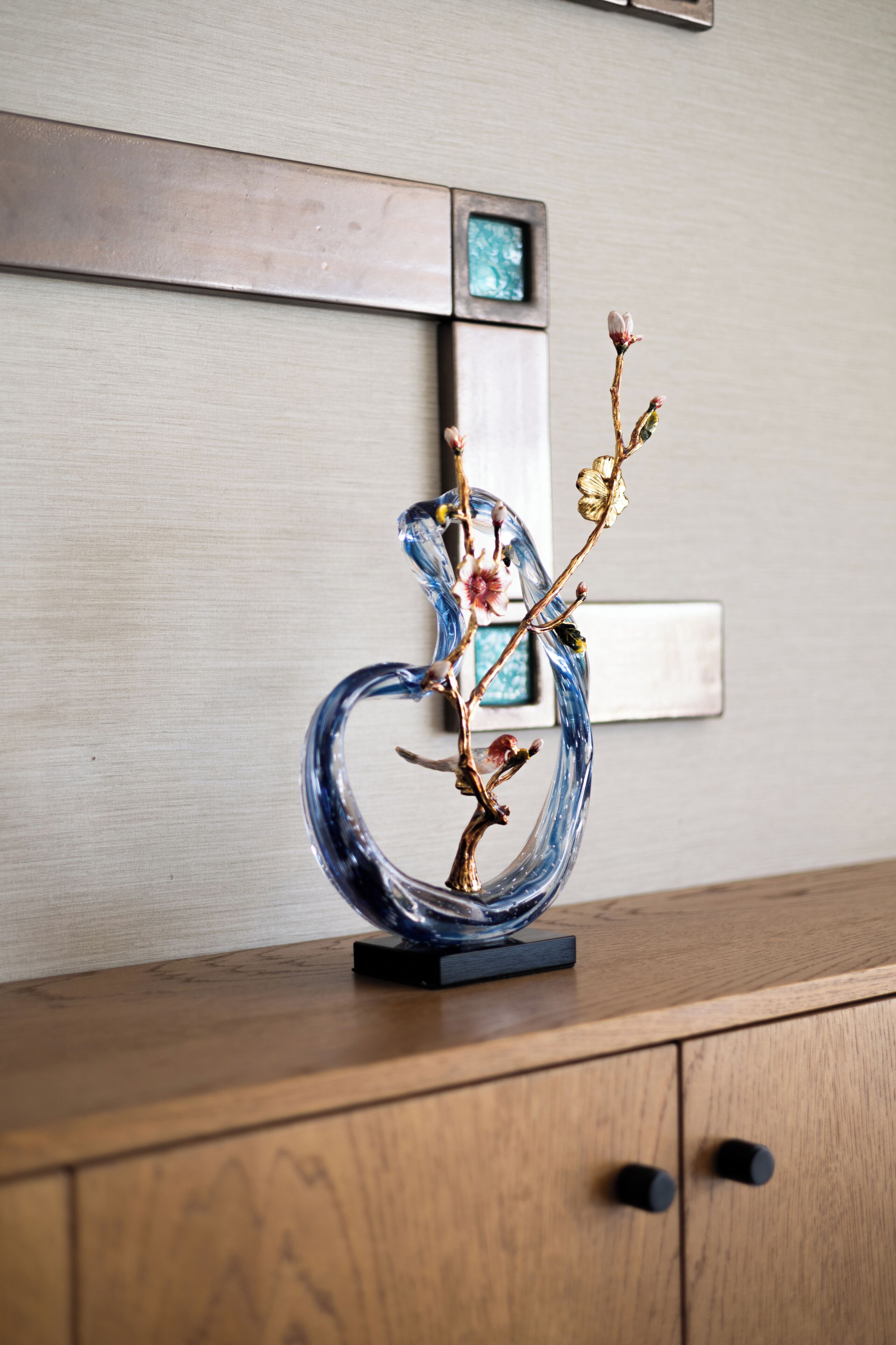 A decorative glass sculpture on a wooden cabinet with a wall-mounted picture frame above.