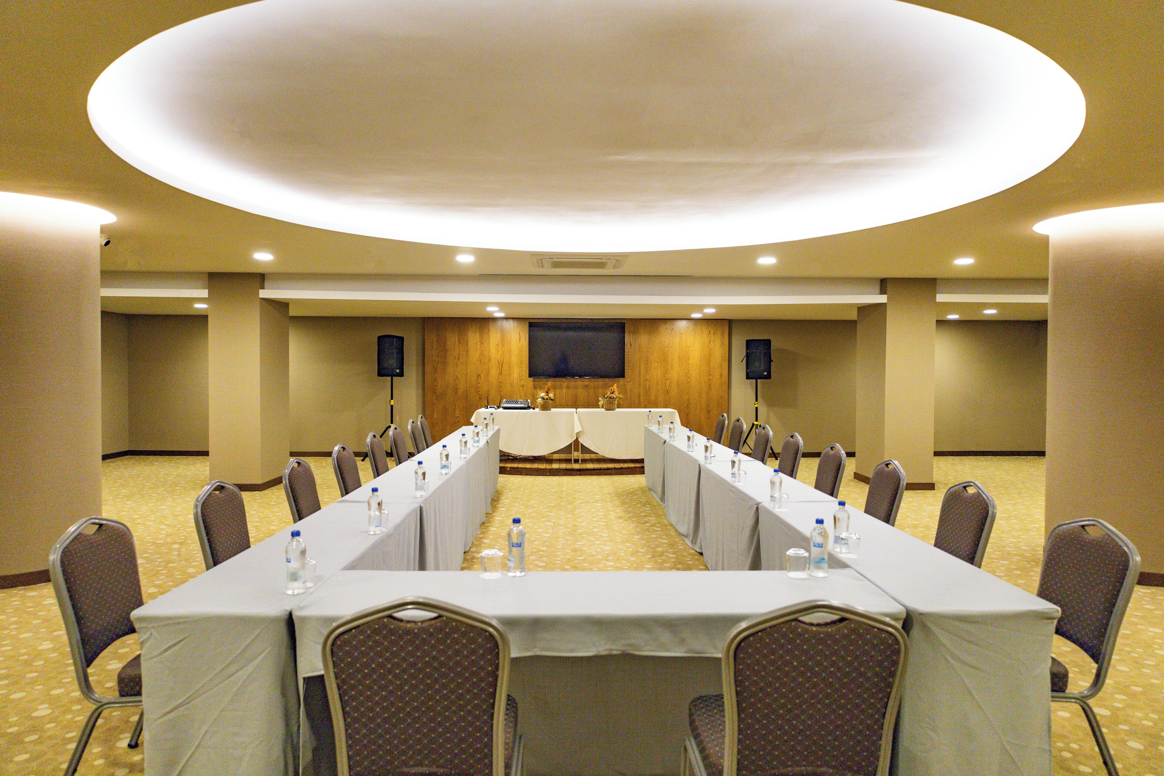 Una sala de conferencias con una larga mesa, sillas, una pantalla de televisión y botellas de agua.