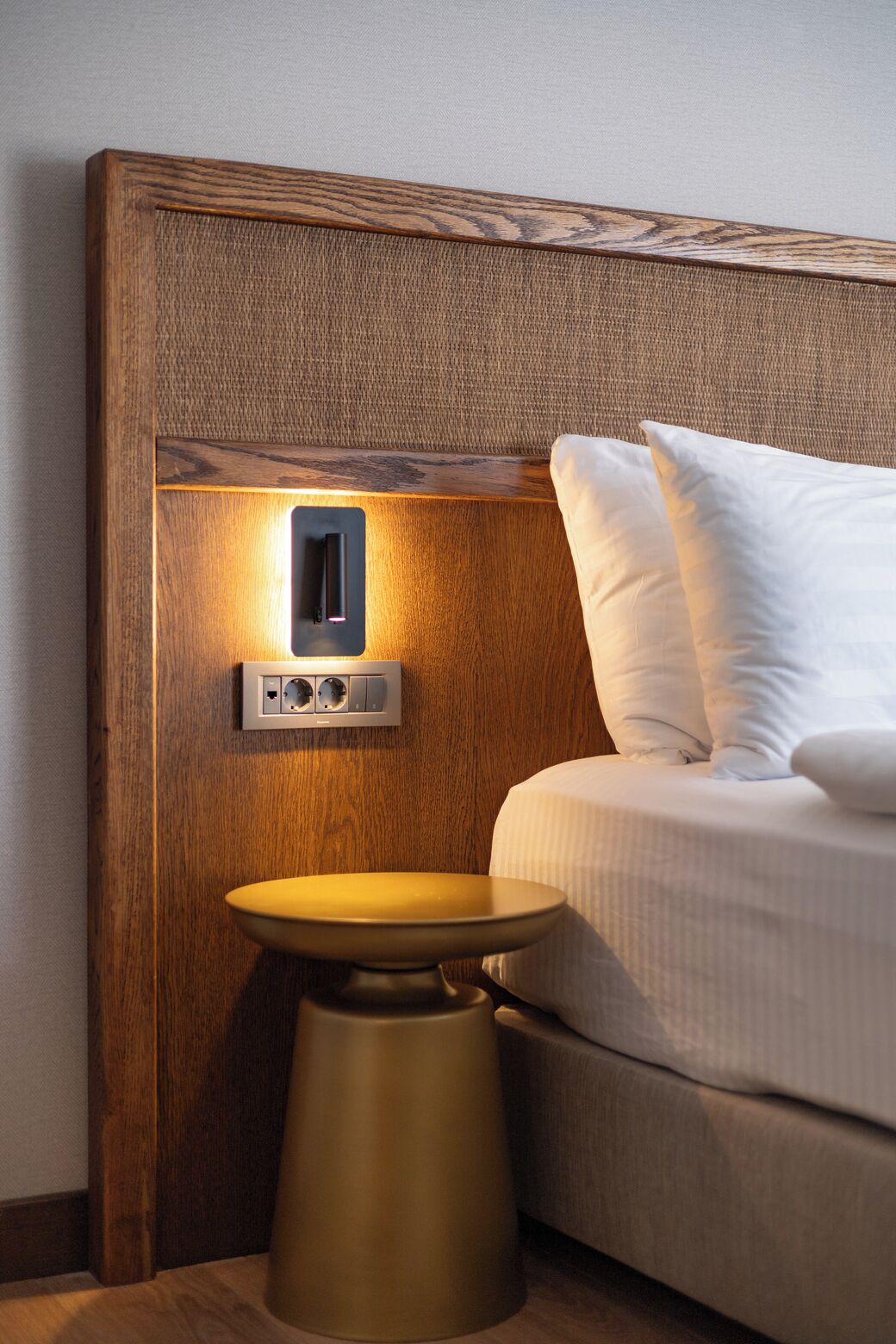 A wooden headboard with a built-in light, a bedside table, and a bed with white bedding.