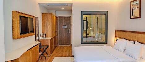 A hotel room with a bed, a desk with a chair, a mirror, a window, and a ceiling fan.