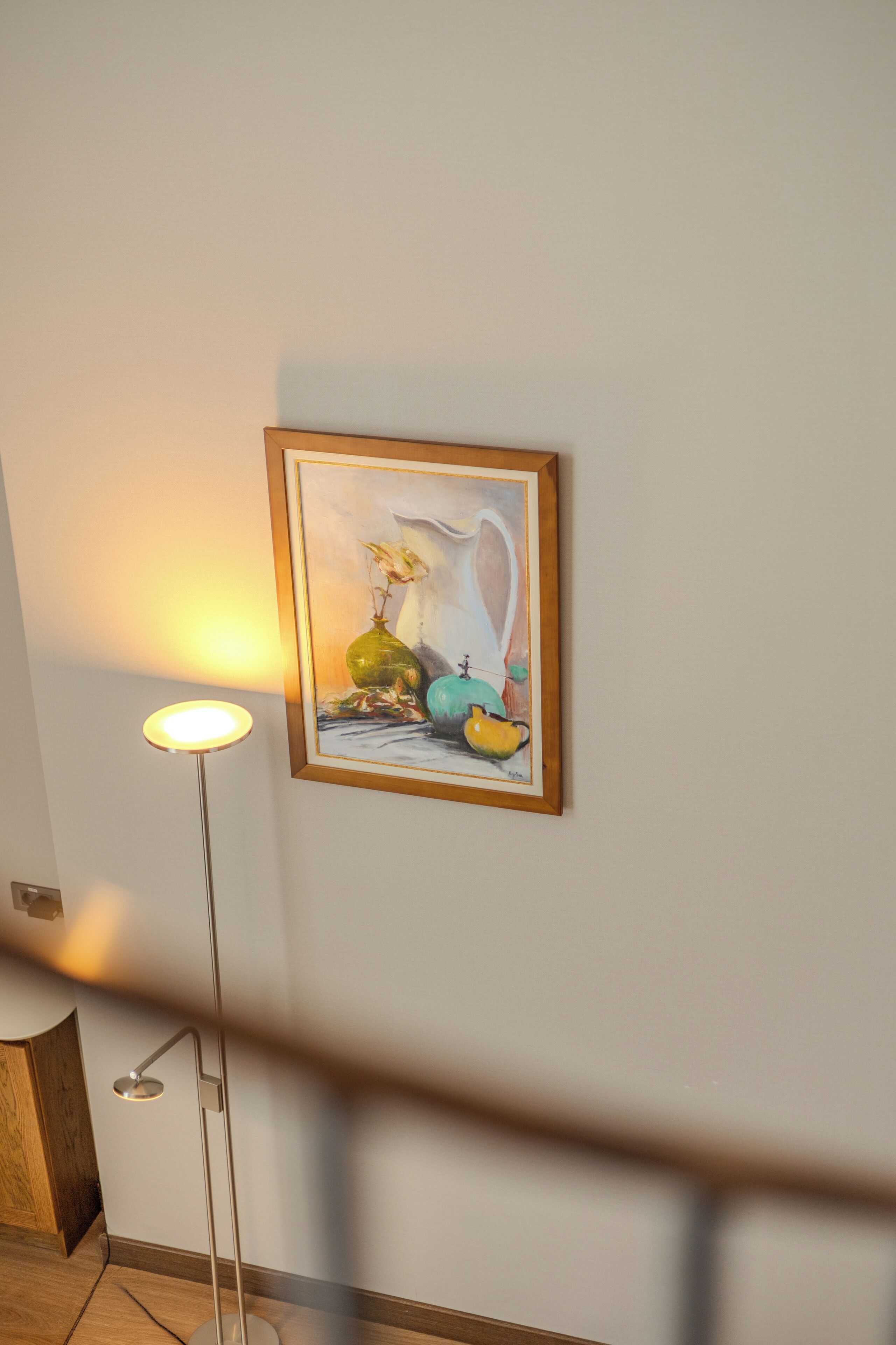 Un cuadro enmarcado en una pared, una lámpara de pie y una barandilla de madera para las escaleras.