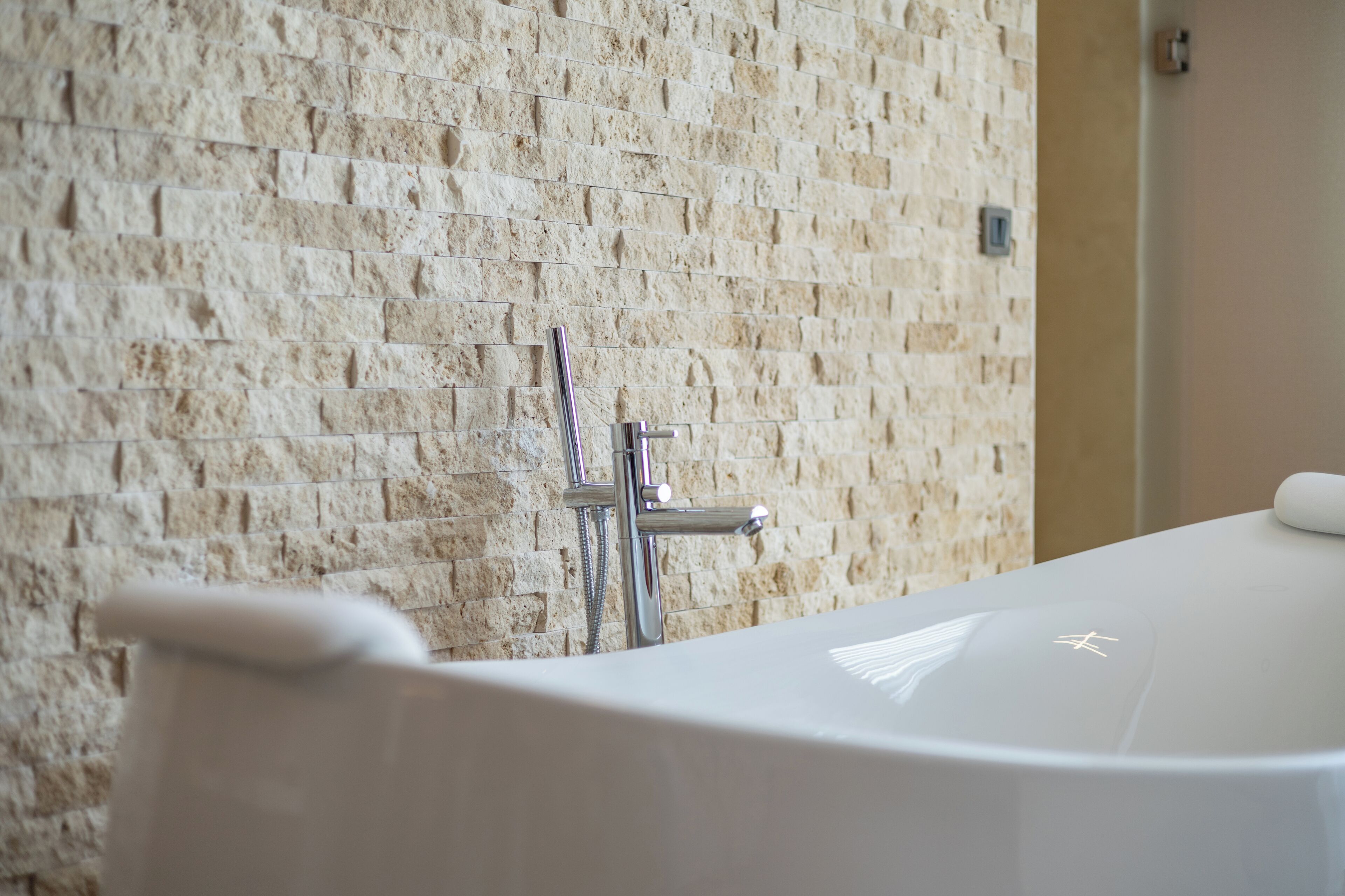 Une salle de bain avec un mur en pierre, une baignoire et une pomme de douche.