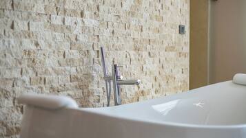 Une salle de bain avec un mur en pierre, une baignoire et une pomme de douche.