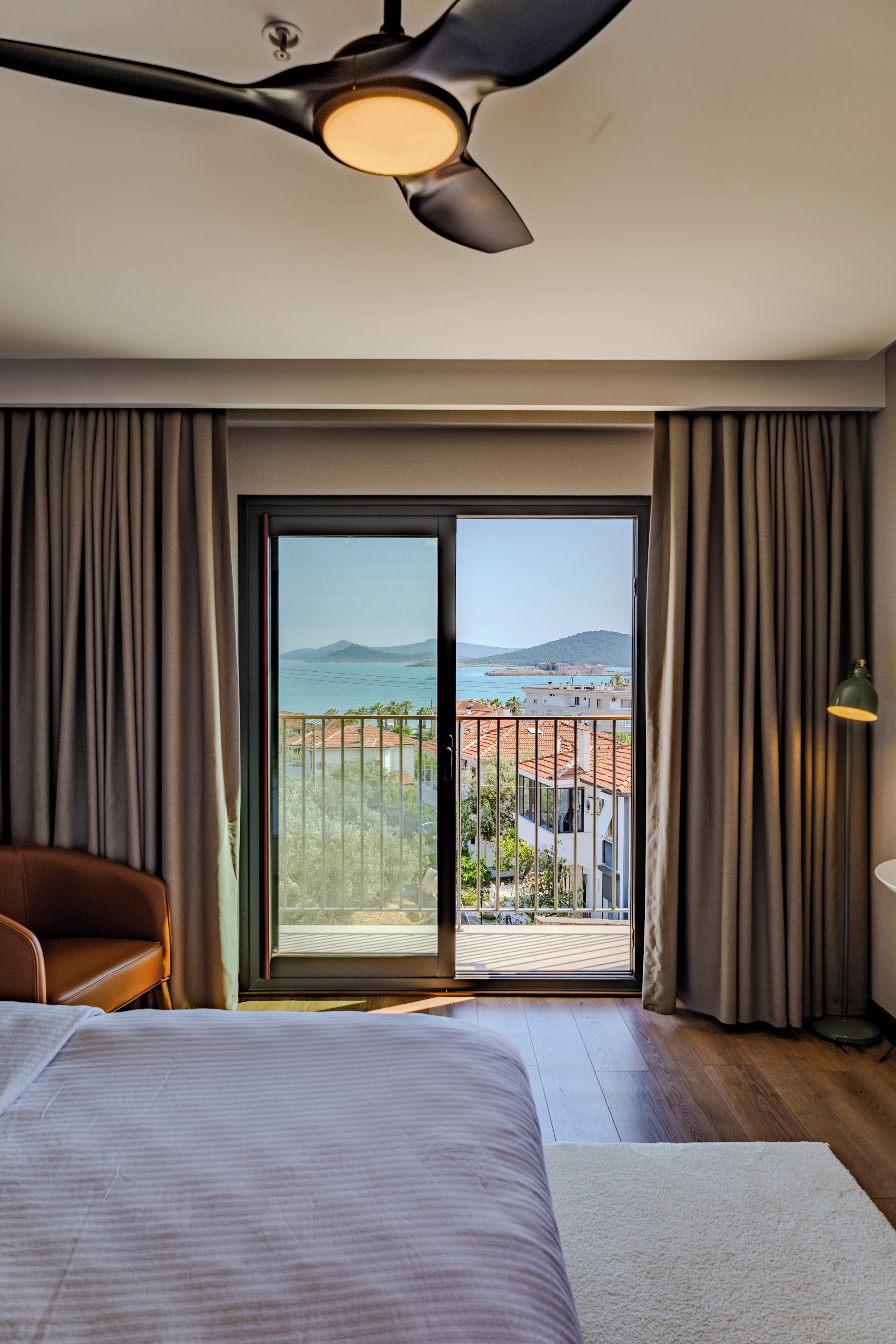 Habitación de hotel con cama, ventilador de techo, vista al mar y balcón.